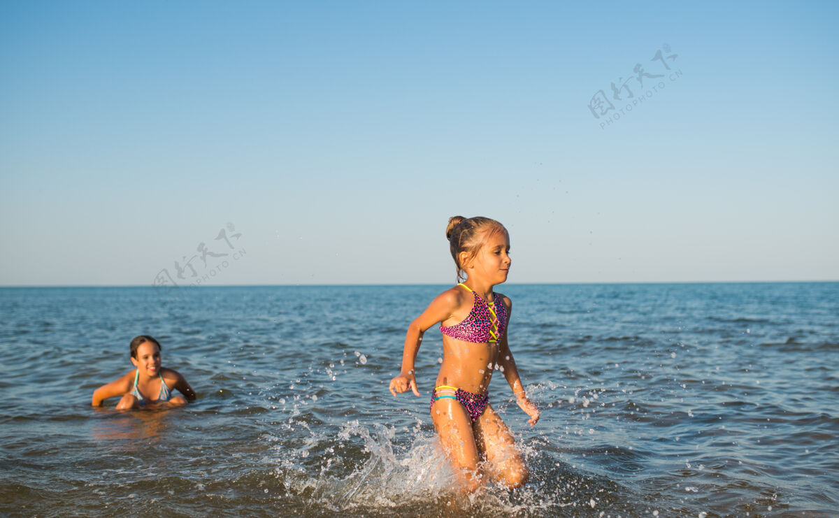 享受在一个阳光明媚的炎炎夏日 两个快乐而积极的女孩姐妹在度假时沿着海浪奔跑年轻泡沫活跃