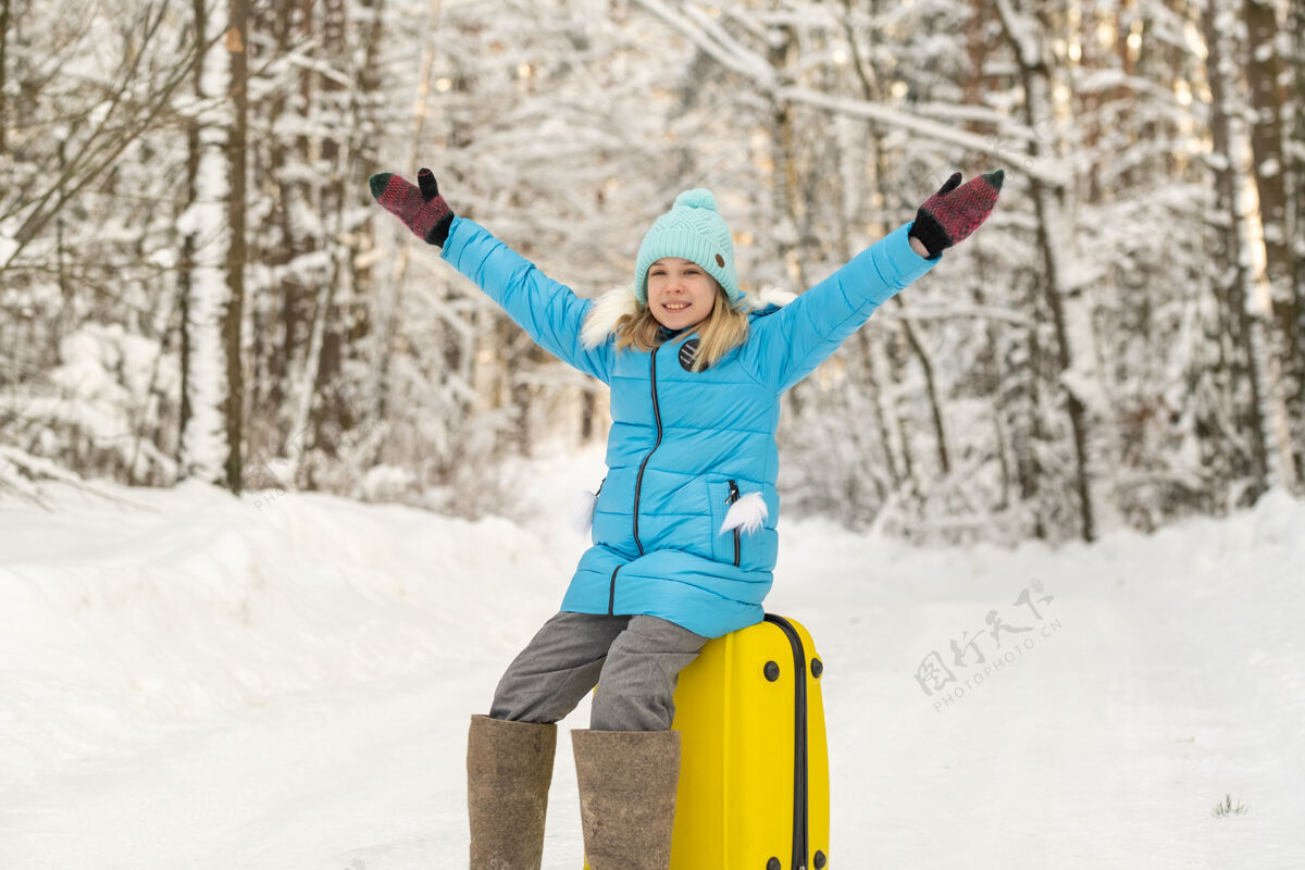 行李冬天 一个穿着毡靴的女孩在一个寒冷的雪天坐在手提箱上包坐着手提箱