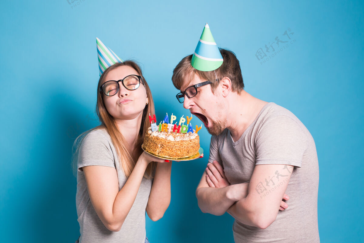 爱一对奇怪的年轻夫妇戴着纸帽子的女孩和男孩想咬下一块祝贺蛋糕疯狂节日庆祝