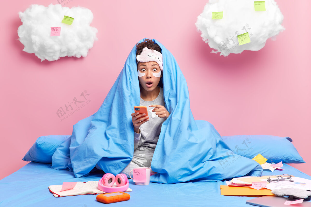 国内毛毯下的女人指着智能手机发现令人震惊的消息闲暇时间在家里戴着睡眠面罩睡衣做作业学习远包装书房指点