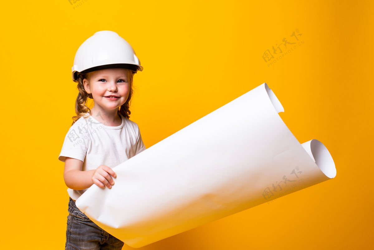 肖像戴着建筑头盔的小女孩建筑师 黄色的墙上贴着隔离的海报建筑工程师可爱