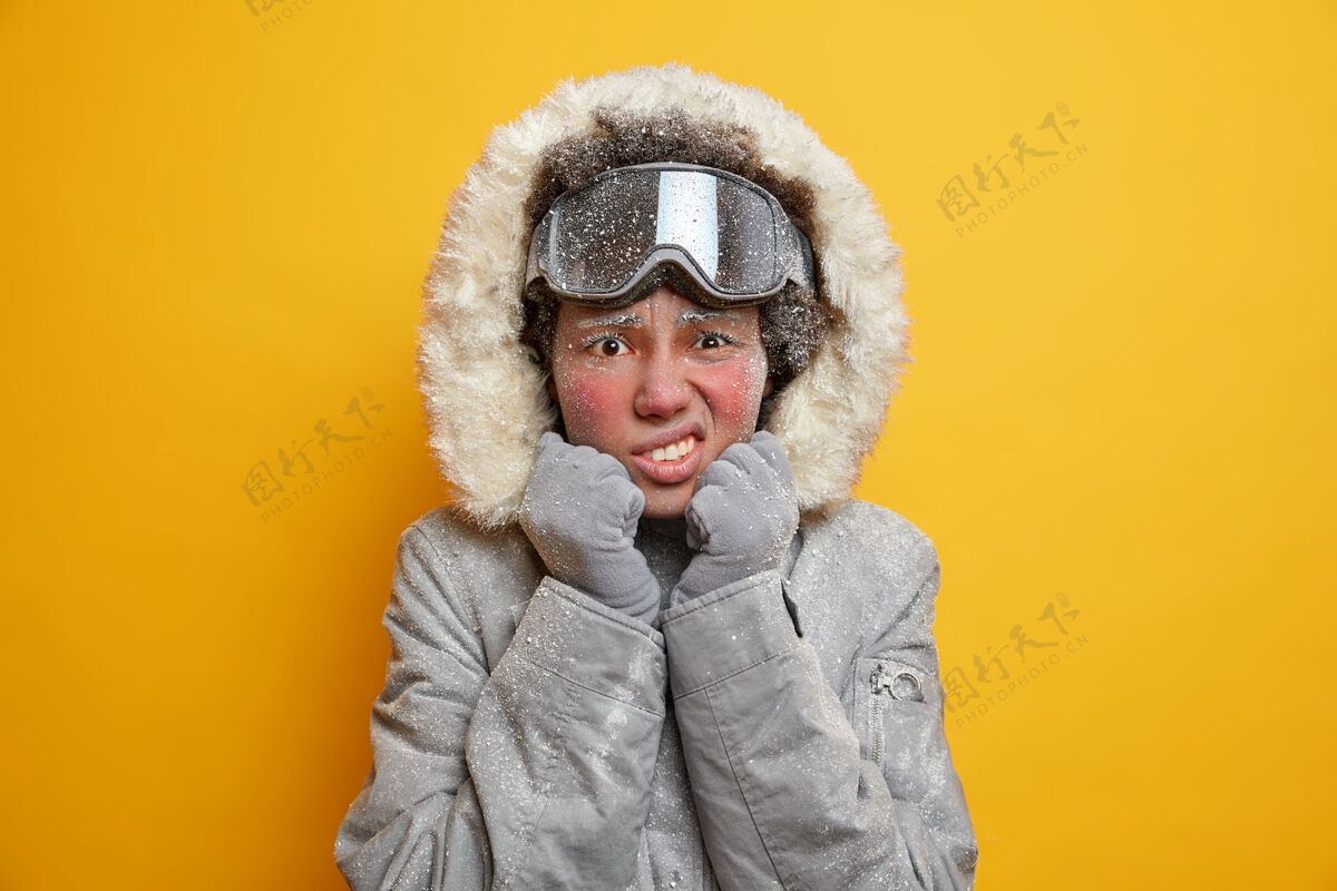 冬天不高兴的非裔美国妇女脸上布满了冰咬紧牙关从寒冷的外观不高兴地穿夹克和滑雪镜享受暑假在寒冷的天气颤抖不满意颤抖冰冻