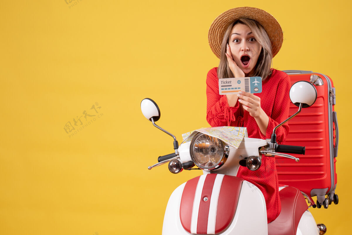 运动一位身着红色礼服的年轻女士手持轻便摩托车的车票 惊艳不已比赛人玩