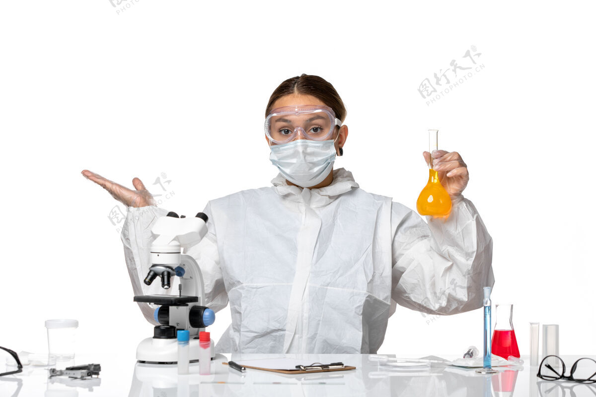 专业人员正面图：女医生 穿着特制的工作服 戴着口罩 白色桌子上放着黄色溶液的瓶子 里面有冠状病毒烧瓶药品面罩