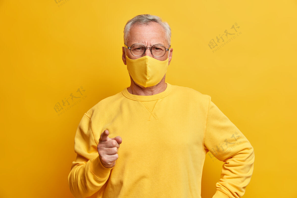 人严肃的白发苍苍的男人表情严肃地看着前面的点食指朝前 戴着黄色的口罩作为室内的防毒面具成熟安全病毒