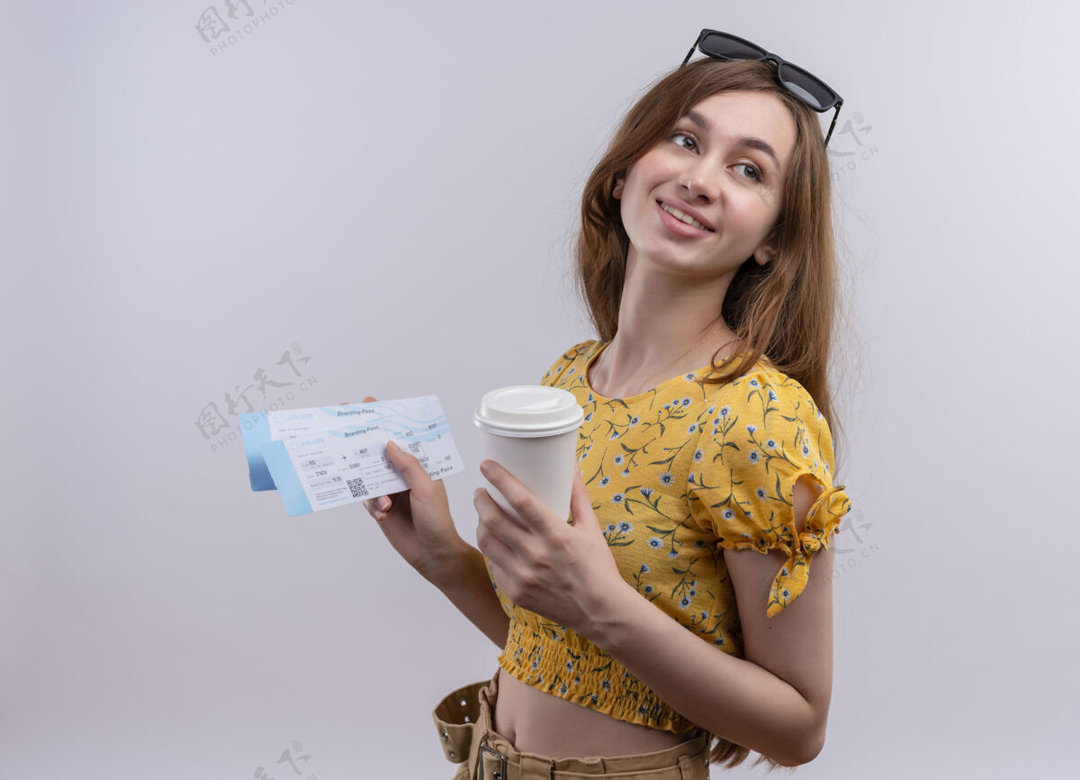 女孩微笑的年轻旅行家女孩头戴太阳镜拿着飞机票 隔着一堵白色的墙上挂着塑料咖啡杯票穿飞机