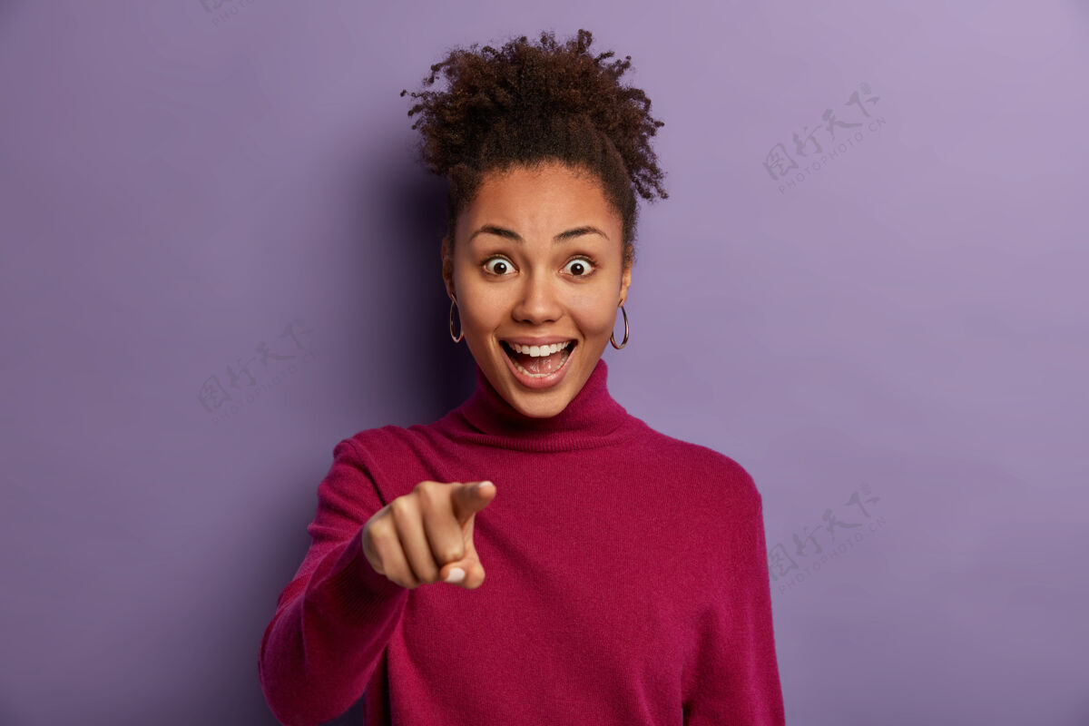 凝视我需要你快乐的卷发少女用食指表示 挑选候选人 有积极的惊讶表情 大笑 在紫色的墙壁上摆姿势 说难以置信搞笑种族卷发