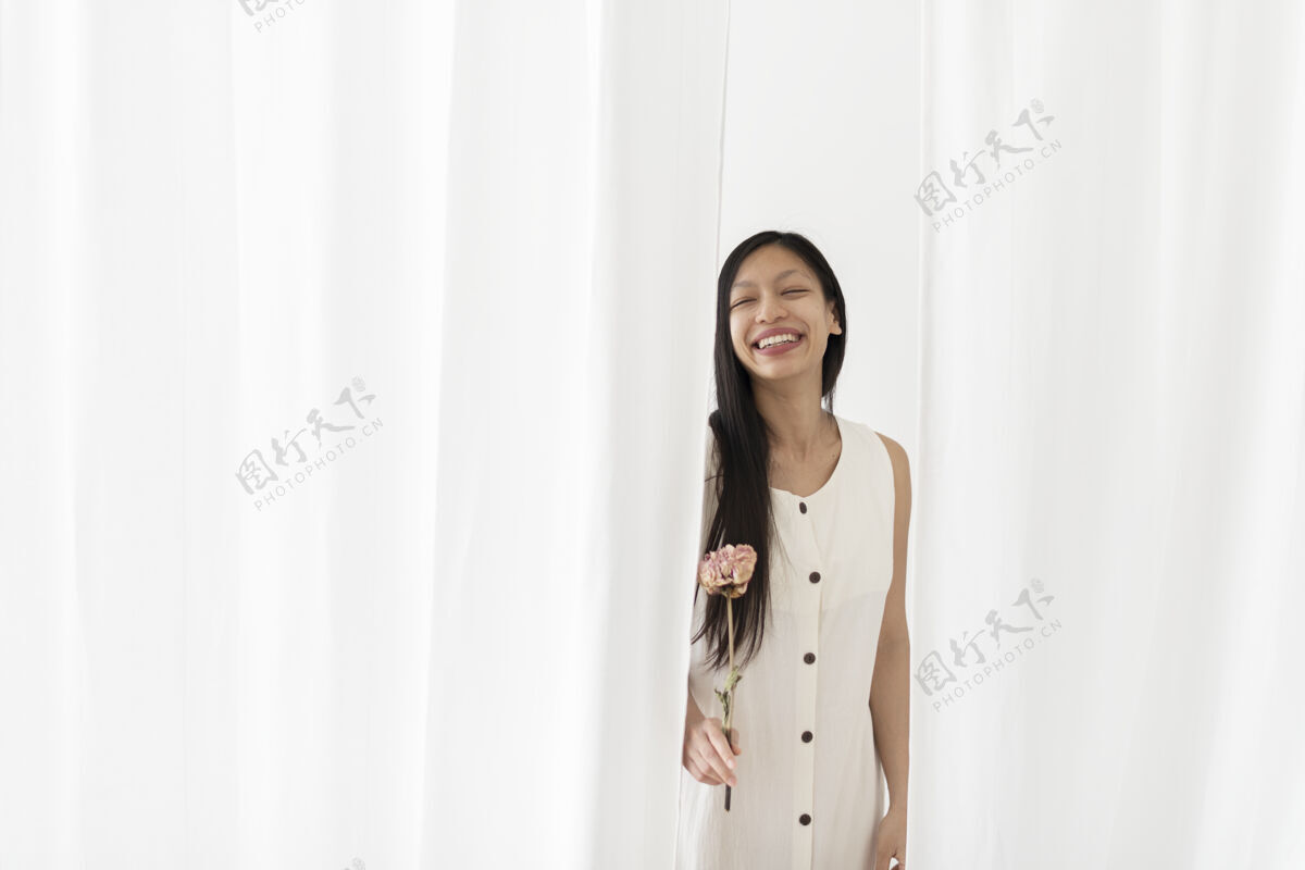 树枝快乐的亚洲女人手里拿着一朵粉色的牡丹花 在白色的窗帘中间家居装饰房间最小