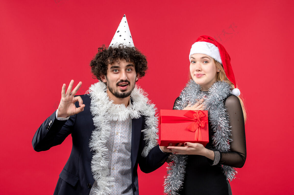 成人正面图：年轻夫妇带着礼物在红墙派对上庆祝圣诞之爱礼物年轻夫妇风景