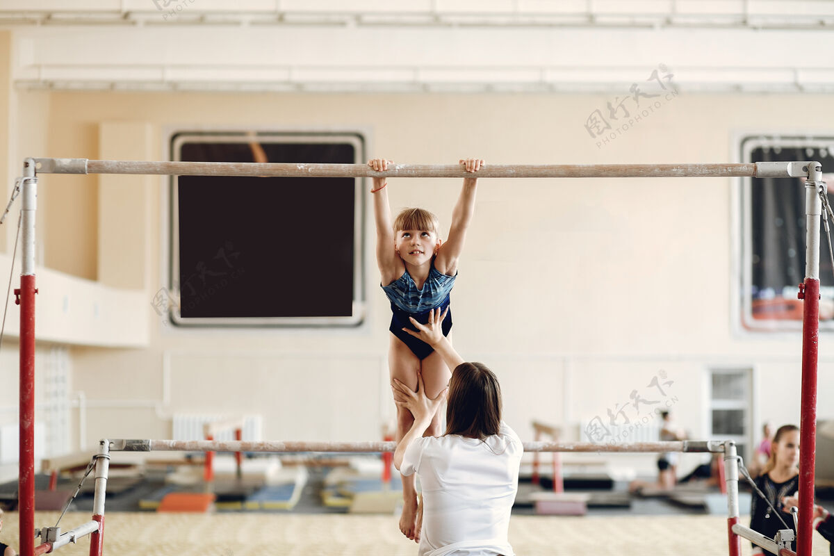 特写儿童体操平衡木女子体操运动员在体操比赛中练习单杠带着孩子的教练开始柔韧性敏捷性