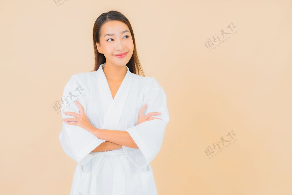 日本肖像美丽的亚洲年轻女子穿着米色的微笑浴袍面部清洁护肤