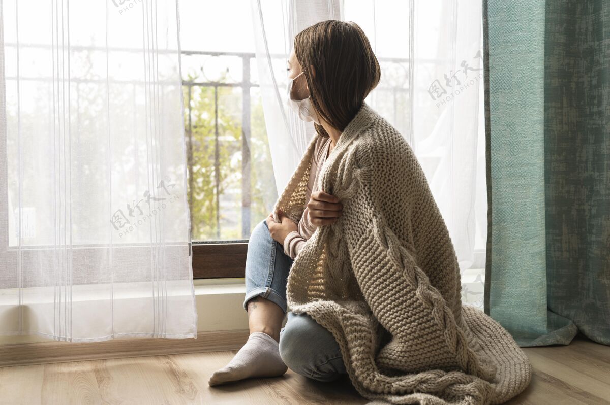 社会在流感大流行期间 一个戴着医用口罩 穿着毯子的女人从窗户往外看预防隔离复制