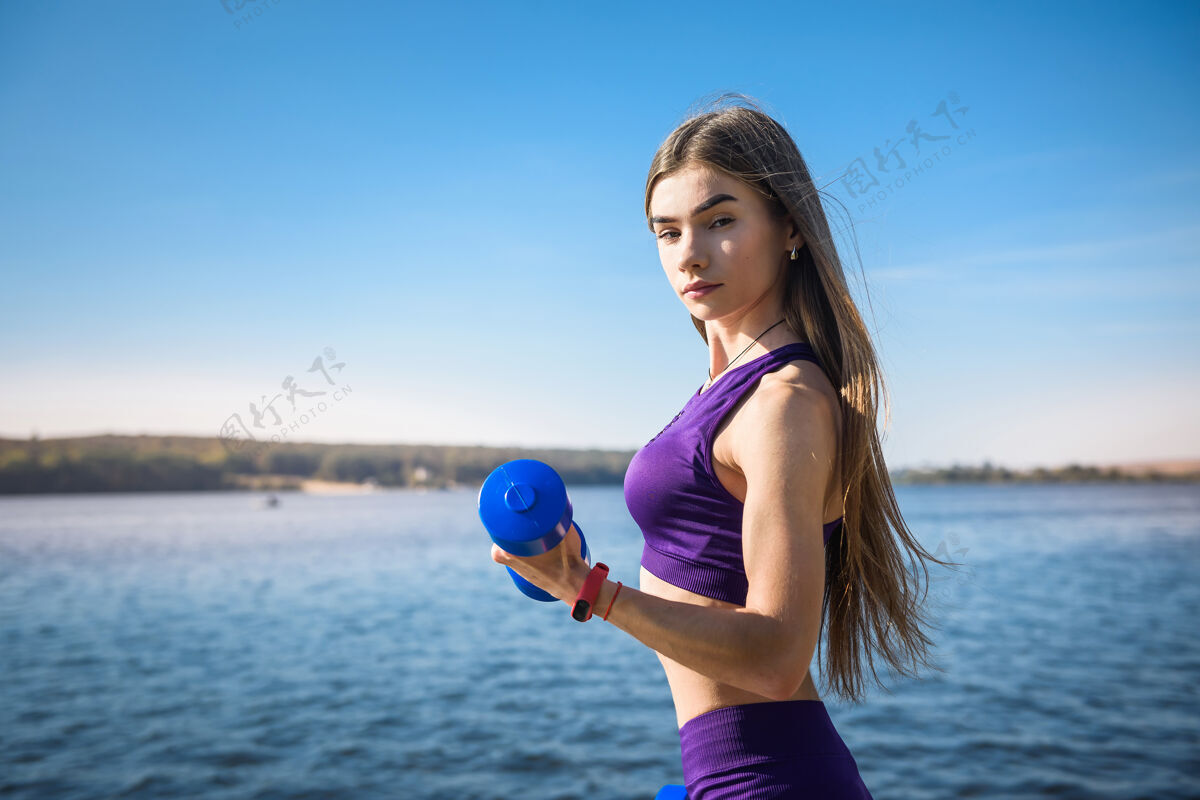 深色在湖边的大自然中 一位手持哑铃的健身女士正在锻炼身体早晨锻炼运动员
