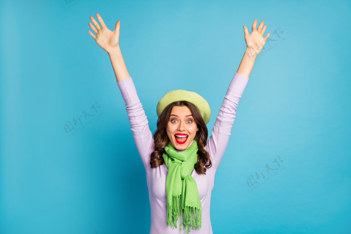 微笑时髦旅客女士举手张嘴兴奋上瘾购物者戴绿色贝雷帽紫色高领围巾隔离蓝色墙壁的销售照片天哪积极冬天