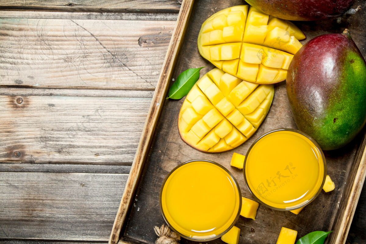 芒果芒果汁放在一个玻璃杯里 放在乡村桌子上的托盘上素食提神营养