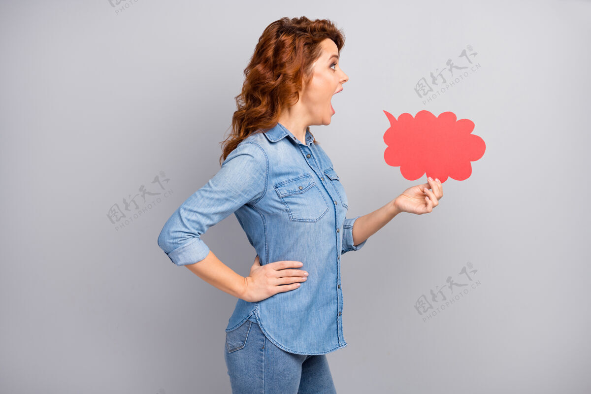 交流侧面照片惊讶的疯女人拿着红色的纸牌泡泡印象深刻的喊叫难以置信的宣传品穿现代服装隔离灰色墙壁告诉说话情绪