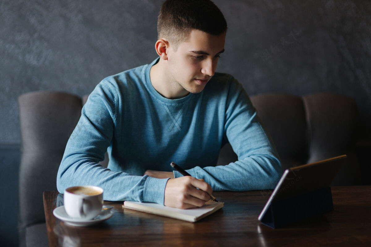 咖啡一个男人坐在咖啡馆里 用平板电脑在笔记本上写下一些东西男人咖啡馆男性