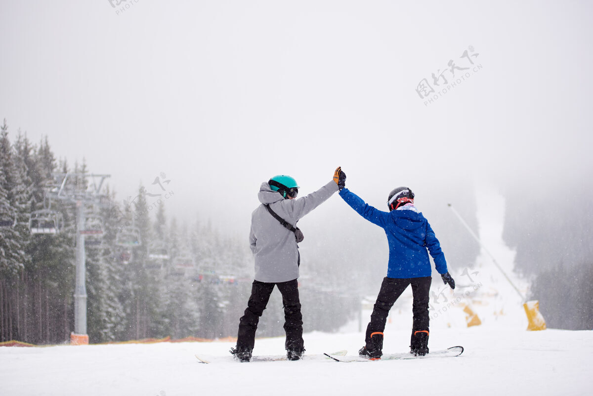 木材一对滑雪板运动员站在滑雪道上击掌浓雾的景色在降雪的背景上娱乐头盔森林