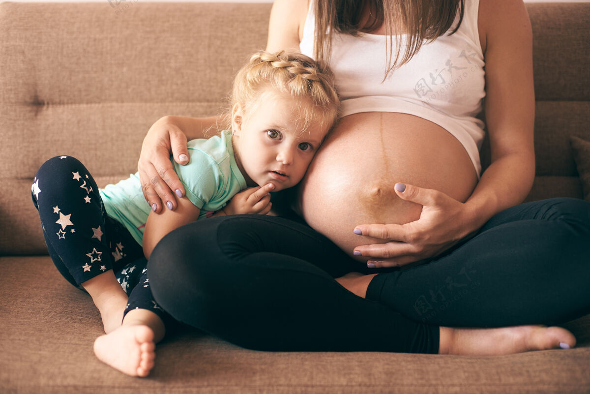 可爱可爱的女孩坐在沙发上与怀孕的母亲的正面视图坐着分娩女儿