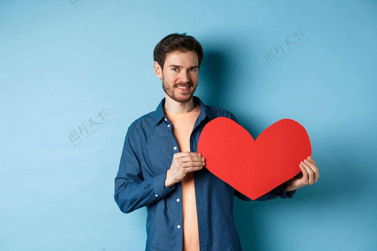 感情情人节快乐的男人 站在蓝色的背景上 展现情人的心和微笑 做一份浪漫的礼物男性礼物丈夫