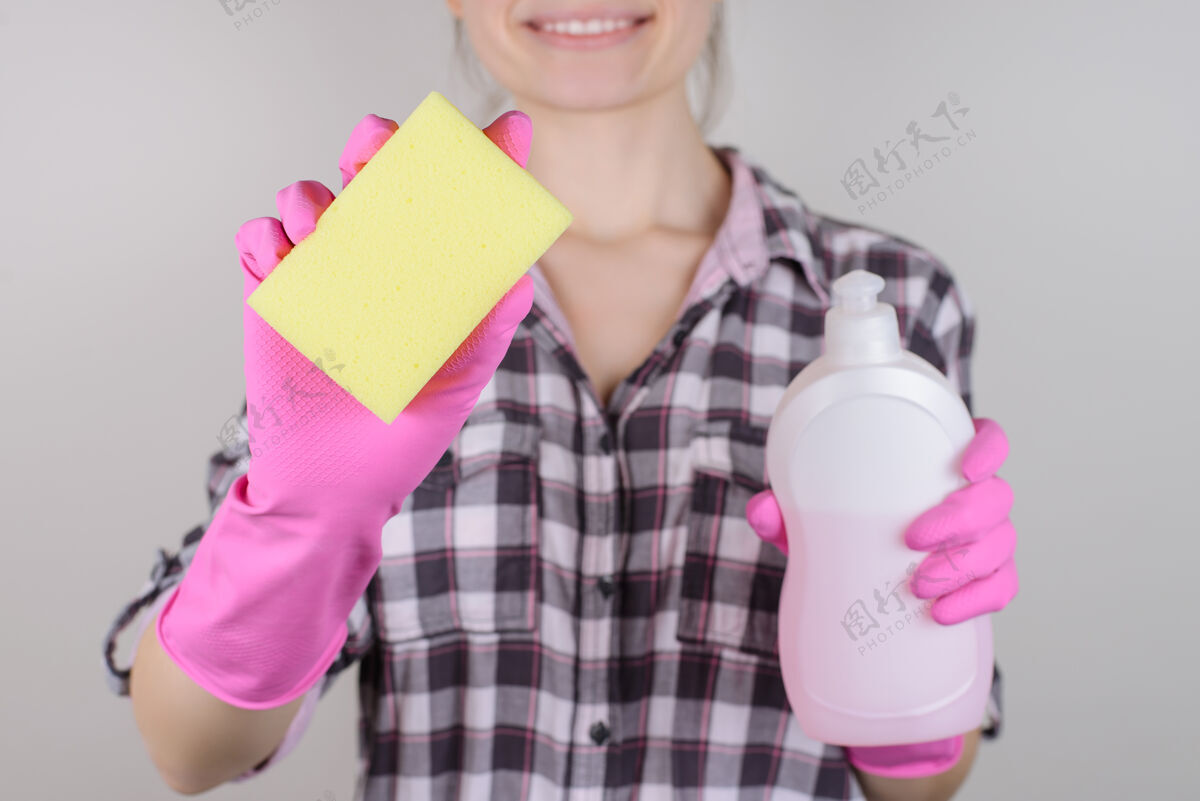 肮脏管家洗碗概念一张开朗自信的女士的特写照片 她拿着黄色的抹布海绵和一个装着粘性化学洗涤剂的瓶子 隔离在灰色的墙上盘子工作人员卫生