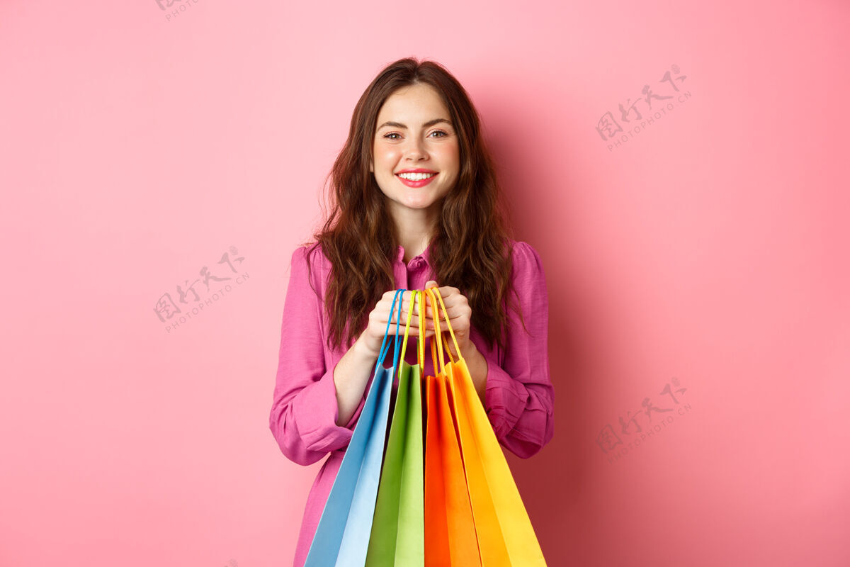 魅力快乐的女士拿着购物袋站着 面带微笑 看上去很快乐 粉色的墙壁女人购物快乐