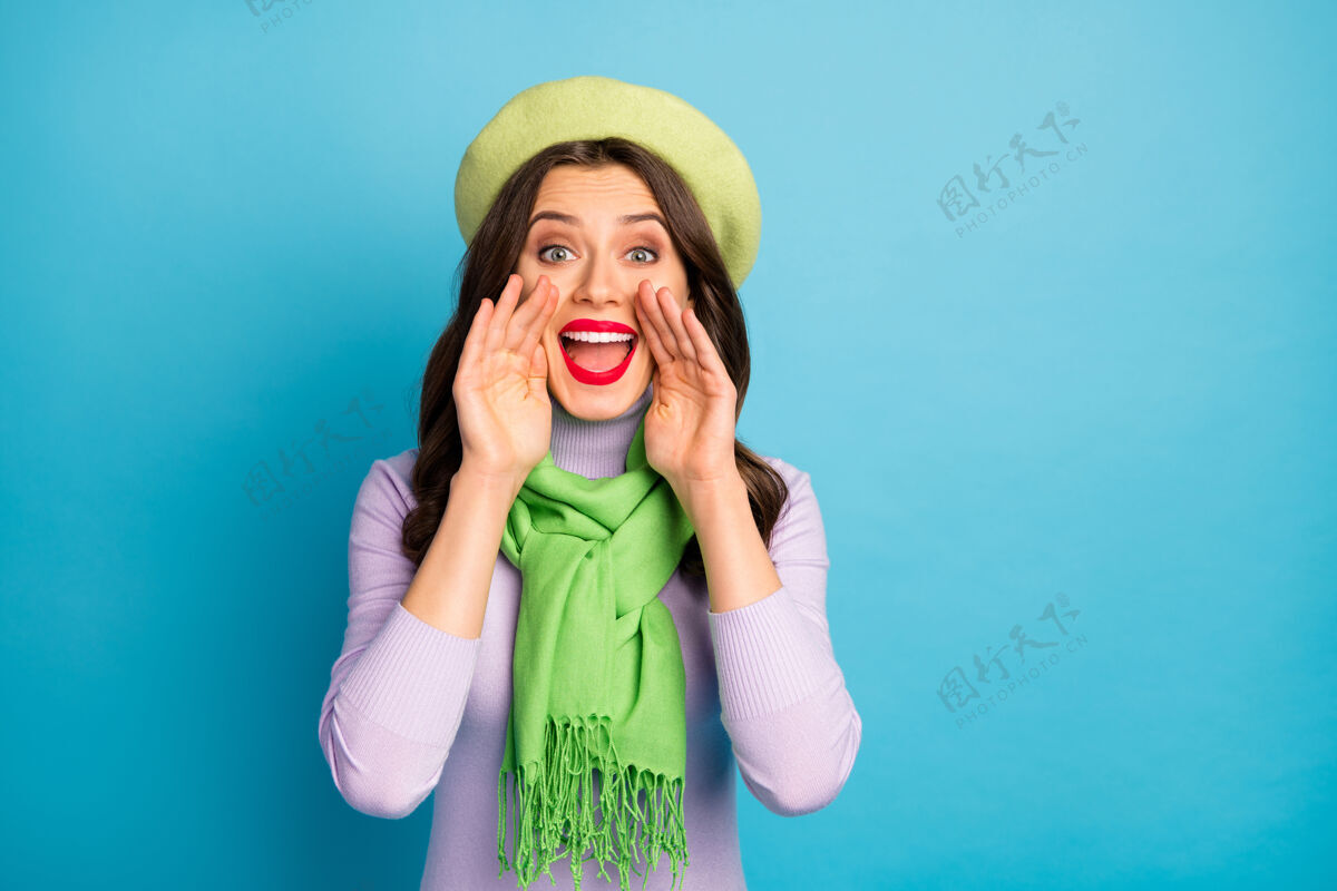 时尚图为酷酷旅行者女士手拉手近嘴尖叫信息卖场购物戴绿色贝雷帽紫色高领套头衫围巾隔离蓝色墙壁围巾沟通信息