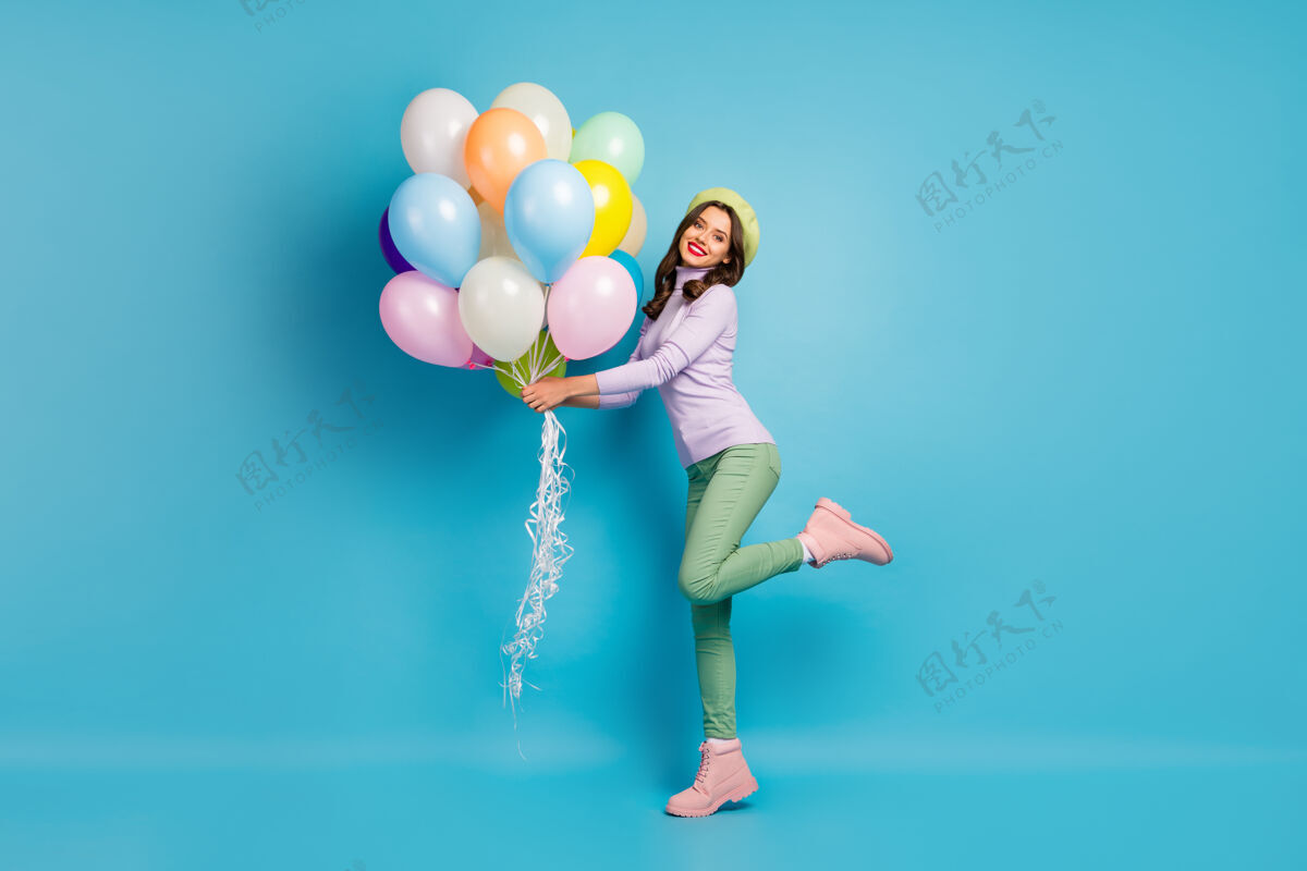 女孩美丽搞笑女士的全身照片带来许多五颜六色的气球朋友活动聚会穿紫色毛衣贝雷帽绿色裤子鞋子蓝色隔离墙女人空气壁板