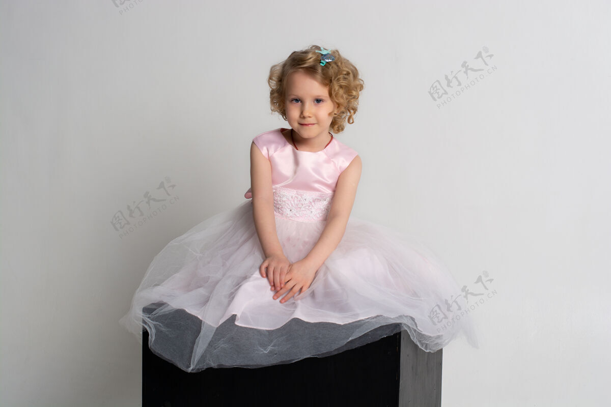 健康一个小女孩穿着粉红色的裙子 头戴皇冠 坐在白色背景的黑色立方体上童年服装人类