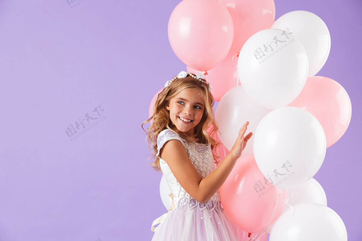 微笑可爱漂亮的小女孩穿着公主裙 隔着紫罗兰色的墙 手里拿着一堆气球白种人庆祝五颜六色