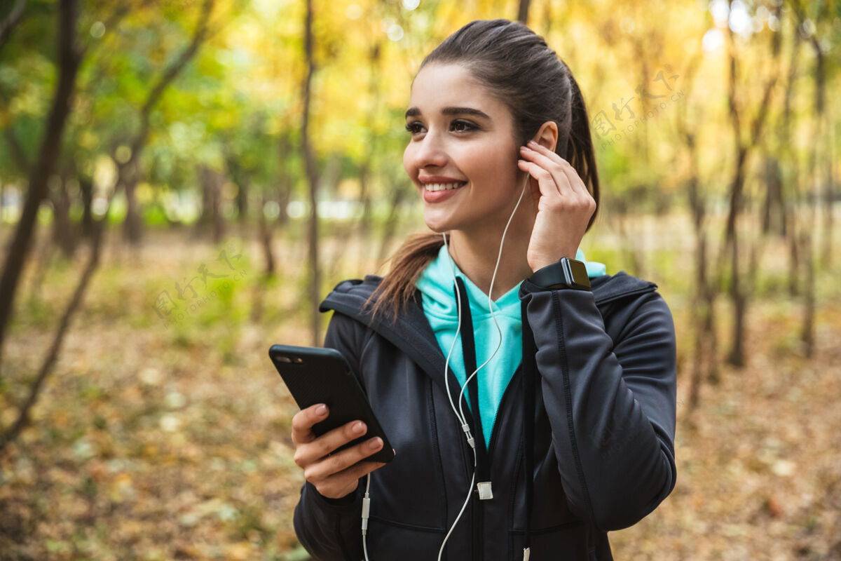 电话照片中 一位年轻漂亮的健身女士在公园里用手机和耳机听音乐女人成人花园