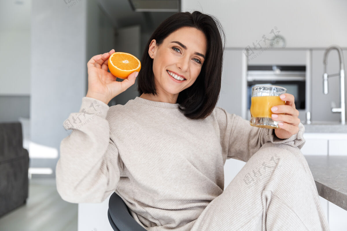 舒适30多岁的黑发女人一边喝着橙汁 一边在明亮的现代房间里休息消遣成熟吸引力