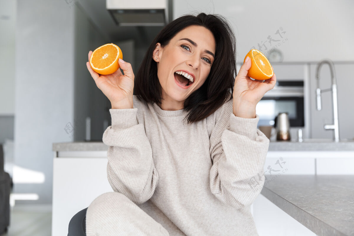 舒适快乐的女人30多岁拿着两片橘子 坐在客厅里肖像满意公寓