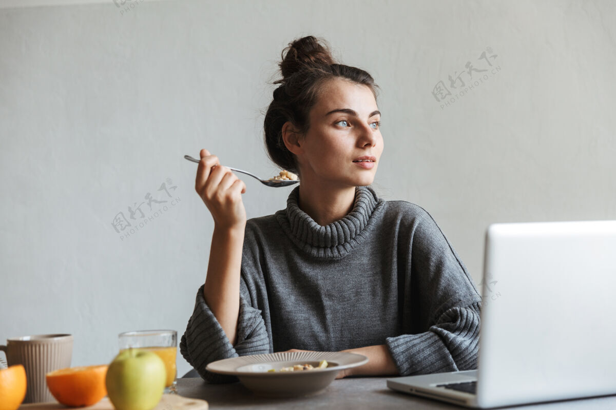 食谱坐在厨房里用笔记本电脑吃健康早餐的年轻漂亮女人水果舒适笔记本电脑