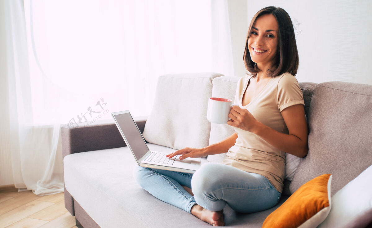 在线自信的现代可爱的年轻女子是在线工作和放松在家里的沙发上与她的笔记本电脑的自由职业者的工作使用生活方式无线