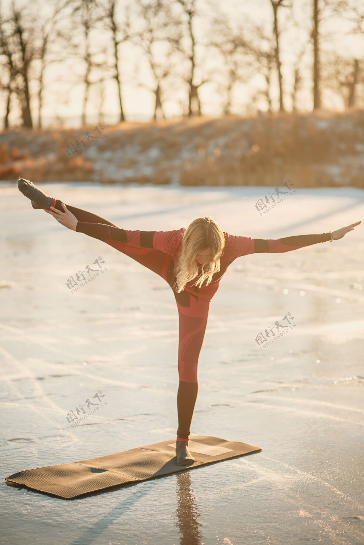 湖冬天 一个女孩在日落时在湖边的冰上做瑜伽运动姿势霜冻