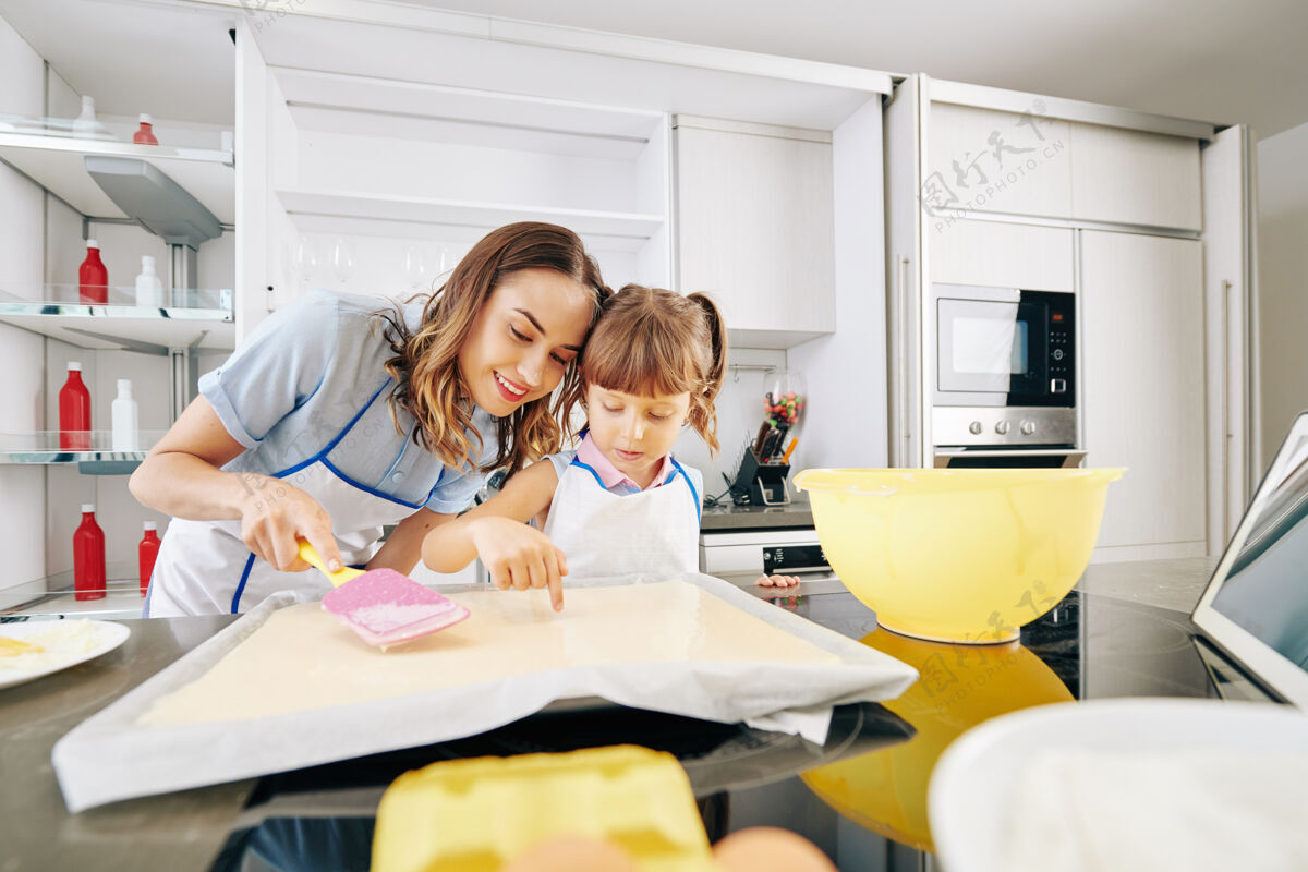 女性带着微笑的妈妈和女儿在检查烤板上的液态面团是否有气泡后代烹饪两个人