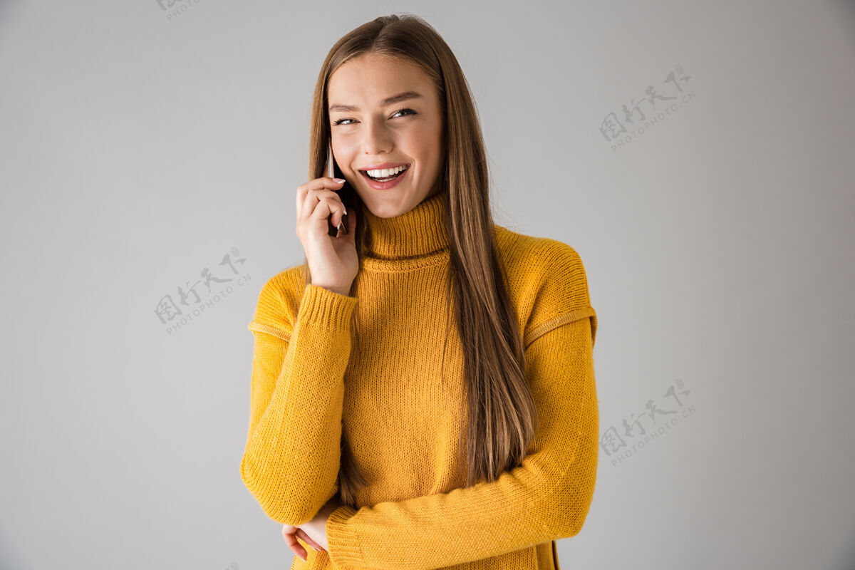 站立一个美丽快乐的年轻女子隔着灰墙用手机交谈的画面白种人休闲毛衣