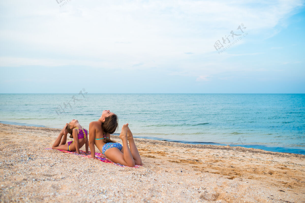 游戏迷人的小女孩在阳光明媚温暖的夏日 一边在沙滩上放松一边做体操伸展海洋运动