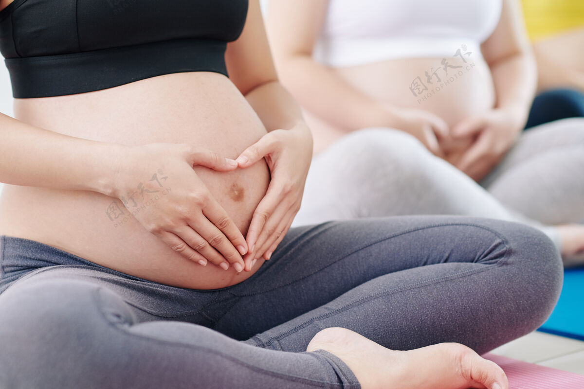 女性特写图片怀孕的年轻女子把手放在肚子上 使心形手标志妈妈身体等待