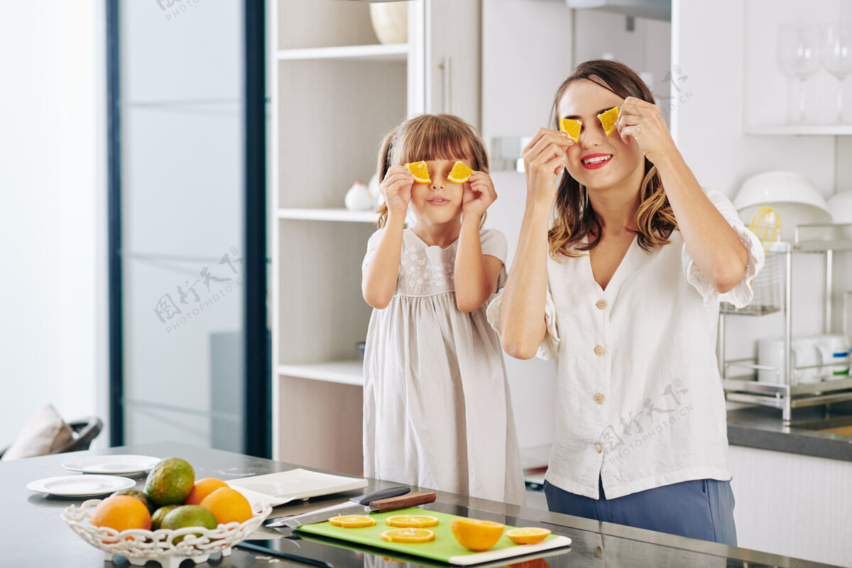 食物和饮料快乐的妈妈和小女儿在厨房柜台摆着橘子片的姿势周末积极的情绪孩子