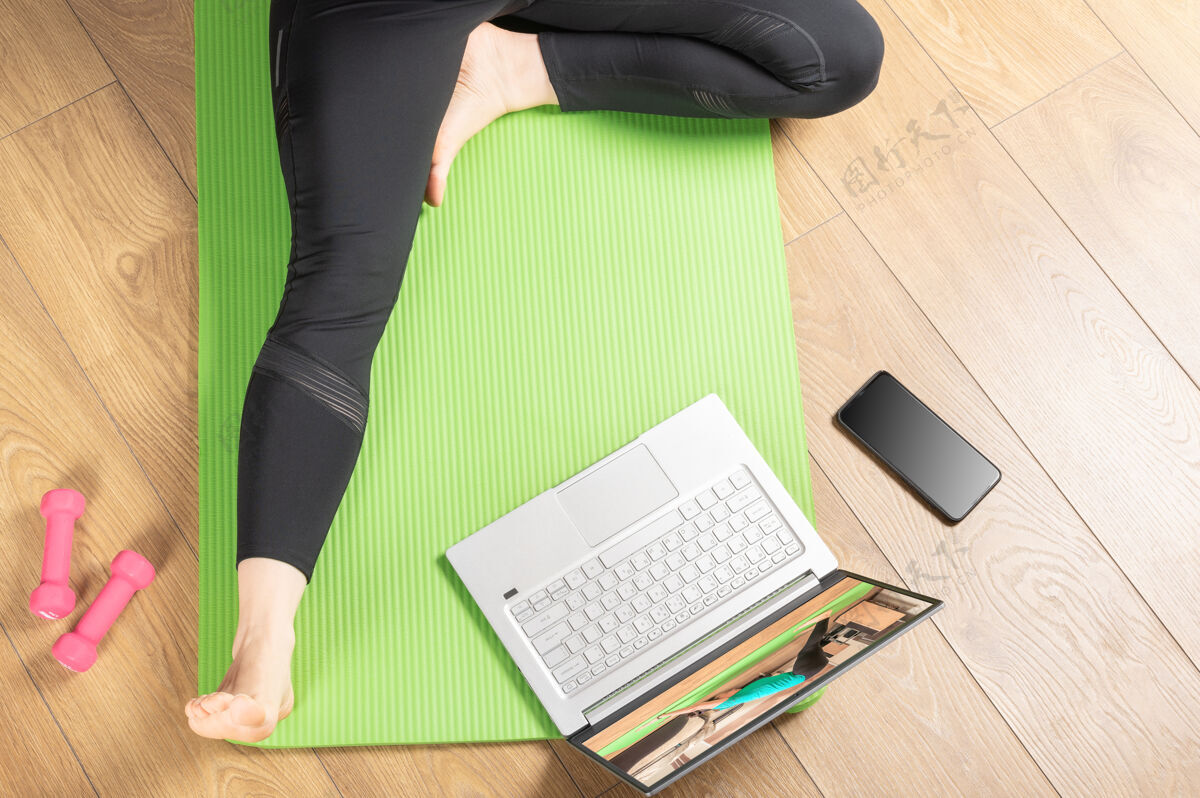 瑜伽姿势这位女士坐在瑜伽垫上 两腿伸开 看着一台白色屏幕的笔记本电脑模型在家里对着笔记本电脑锻炼的女人视频视频会议微笑