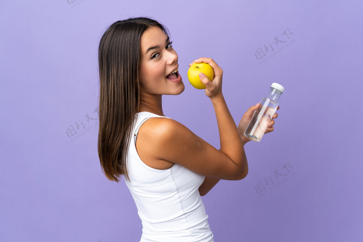 纯净穿紫色衣服的少女拿着一个苹果和一瓶水健康好女人