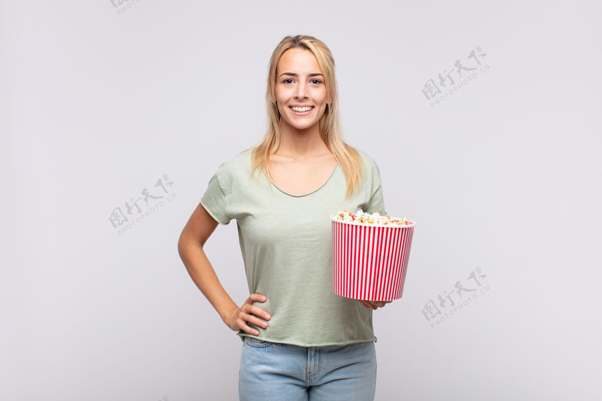 美丽一个拿着爆米花桶的年轻女子 手放在臀部 面带微笑 态度自信 积极 自豪 友好电影院快餐电影