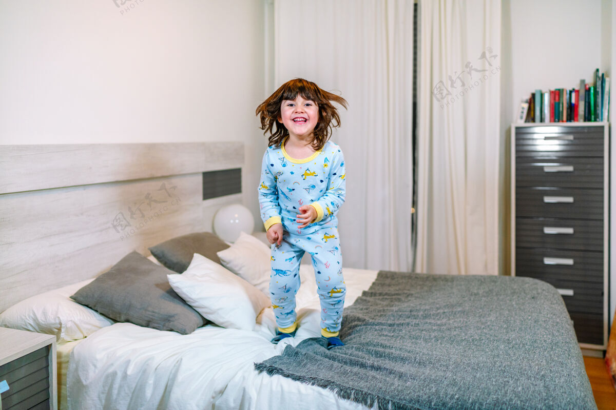房间孩子很高兴在睡觉前穿着睡衣跳到床上孩子爱房子