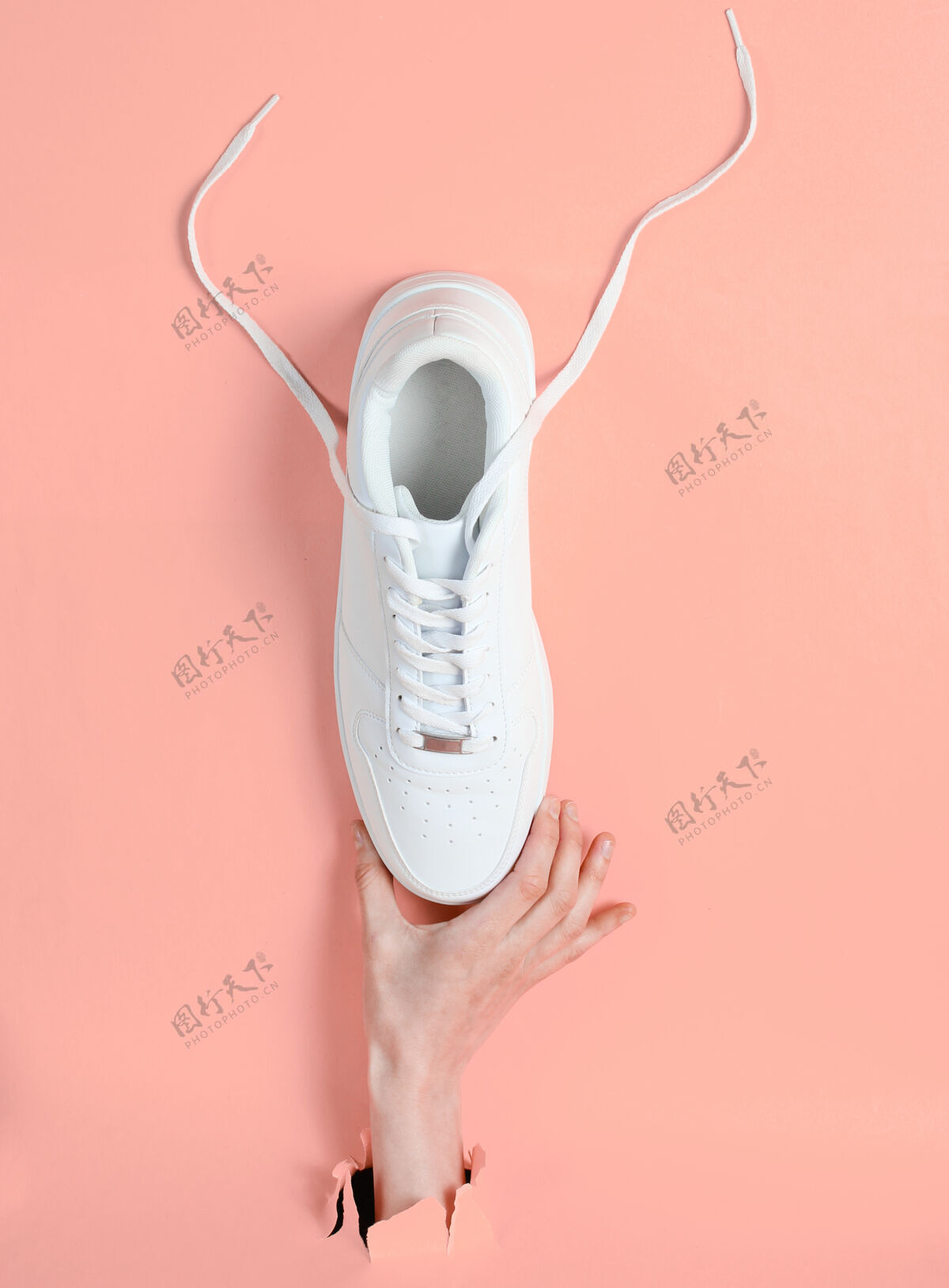 商店女性手拿白色运动鞋穿过撕破的粉色纸简约创意时尚理念青少年运动创意