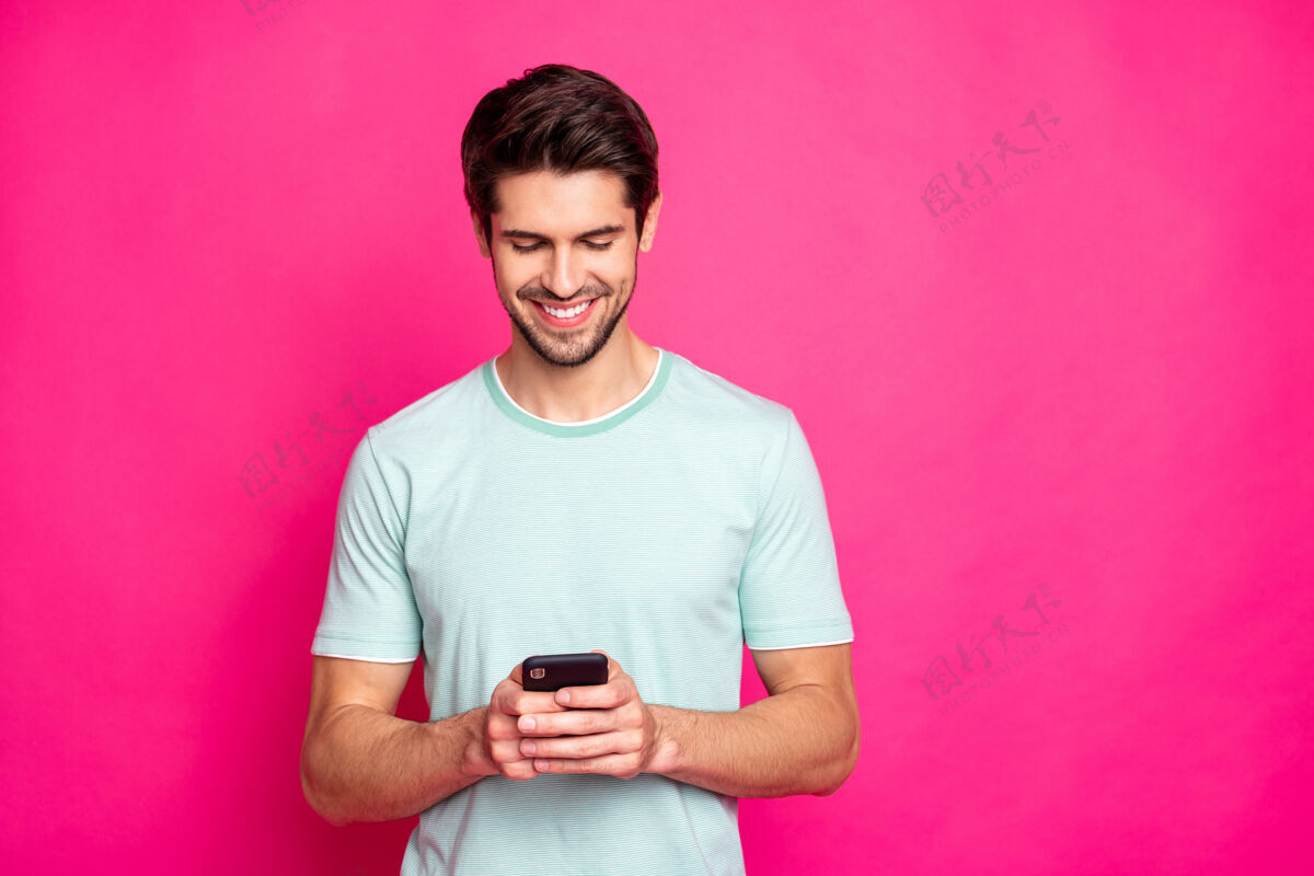 时间照片中的博主手里拿着电话检查订阅者牙牙学语微笑着穿休闲装孤立生动的粉红色背景模特男人搜索