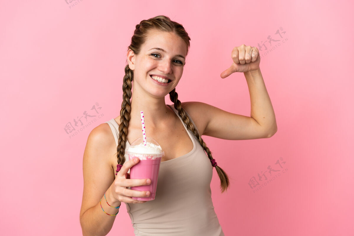 胜利年轻女子用草莓奶昔隔离在粉红色的背景自豪和自我满足满意年轻年轻