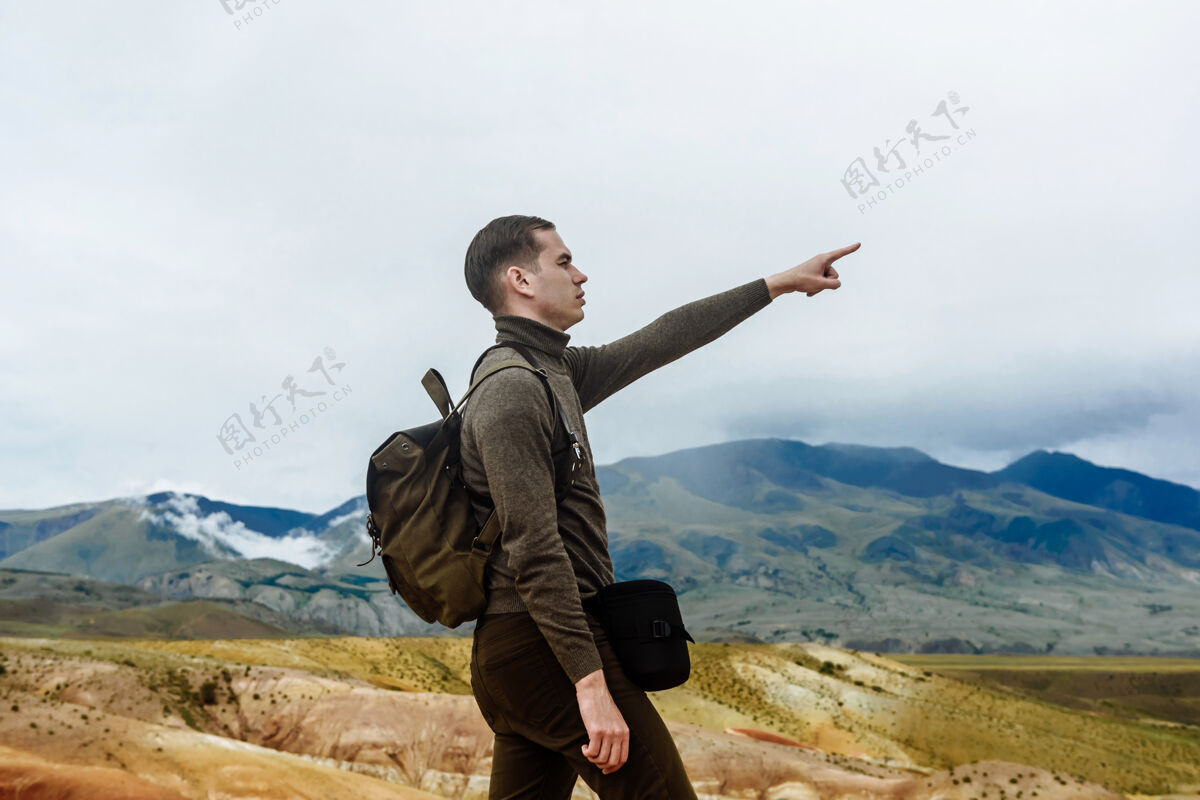 年轻人一个手举背包的年轻徒步旅行者指着远处人男性徒步旅行者