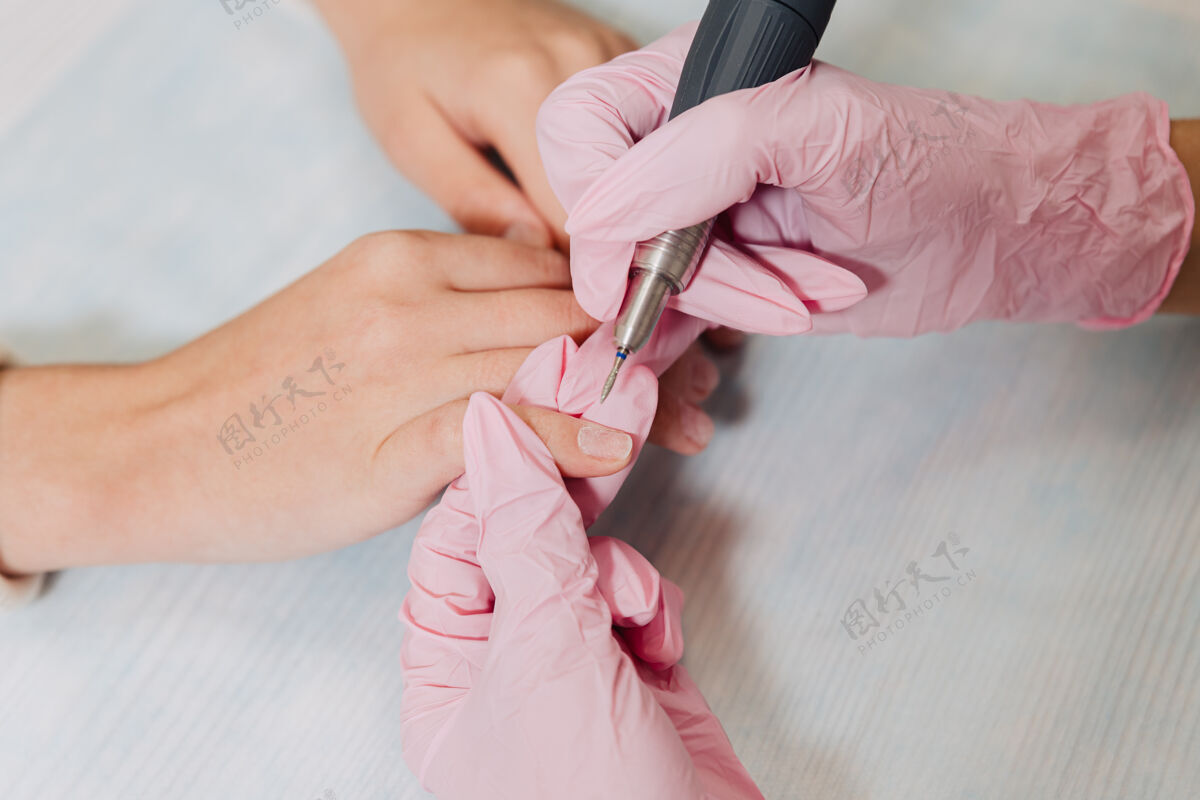 手套修指甲的过程一位戴着粉色橡胶手套的大师用电动指甲打磨指甲文件.female把手收起来电美甲研磨